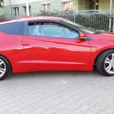 Czerwone Honda CRZ z czarnym dachem stoi na chodniku.