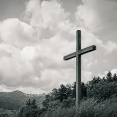 Drewniany krzyż na tle burzowych chmur, symbolizujący nadzieję i eschatologię. W oddali góry i las.