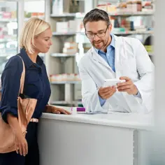 Farmaceuta w białym kitlu pokazuje klientce opakowanie leku, być może na aspargan.