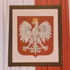 Obraz przedstawia godło Polski – białego orła w koronie na czerwonej tarczy. Dzieło oprawione w ciemną ramę, zawieszone między biało-czerwonymi zasłonami.