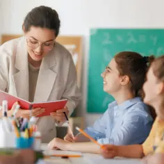 Nauczycielka z zeszytem rozmawia z uczennicą. Czy w 6 klasie jest technika? Tak, to lekcja, gdzie dzieci uczą się nowych rzeczy.