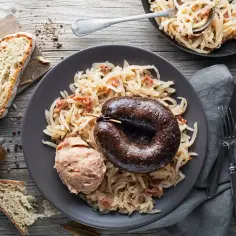 Kaszanka z grilla z kapustą kiszoną i boczkiem, podana z chlebem i pasztetem.