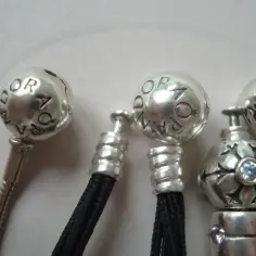 Srebrne zawieszki z logo Pandora, niektóre na czarnych sznurkach. Czy pandora się rozciąga? Nie, to tylko ozdoby.
