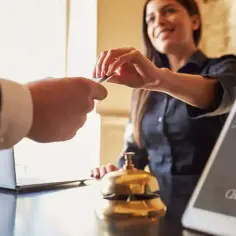 Recepcjonistka uśmiecha się, odbierając kartę od gościa. Na ekranie tabletu widnieje opcja "Check Out", czyli jak się wymeldować.