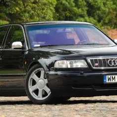 Elegancki, czarny Audi A8 D2 4.2 z lat 90. na brukowanej drodze, otoczony zielenią.