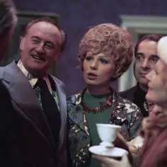 Uśmiechnięty mężczyzna w garniturze rozmawia z kobietą w kręconych włosach. To scena z filmu "Kochaj albo rzuć" z udziałem jego obsady.