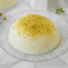 Delikatna zupa nic, kremowa masa z posypką z pistacji na ozdobnym talerzyku, obok stokrotki.