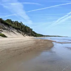 Plaża z wydmami porośniętymi sosnami, w oddali morze i błękitne niebo z chmurami. Miejsce idealne na spacer, jak w orzechowo.