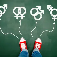 Czerwone trampki na tle tablicy, gdzie strzałki prowadzą do symboli płci i trans. Czy to droga do akceptacji, czy HOcd?