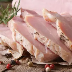 Pokrojony, **super delikatny i soczysty schab gotowany**, przyprawiony pieprzem, z gałązką rozmarynu na drewnianym blacie.