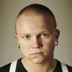 Mężczyzna z krótkimi włosami i kolczykami w uszach i ustach.