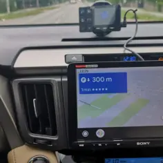 Na ekranie Android Auto widać nawigację Yanosik z informacją o 300 m do celu. W oddali radiowóz.