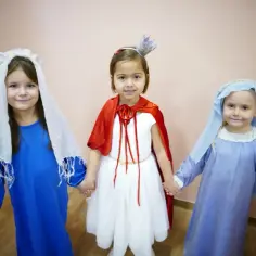 Dzieci w strojach świętych, trzymając się za ręce, tworzą małe kółko.