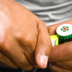 Dłonie otwierające butelkę piwa Heineken kluczem.