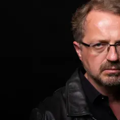 Przemysław Borkowski z Kabaretu Moralnego Niepokoju w czarnej skórzanej kurtce i okularach, zamyślony.