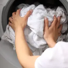 Ręce wkładają białe pranie do pralki. Dowiedz się, dlaczego białe ubrania szarzeją po kilku praniach i jak temu zapobiec.