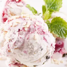 Pyszne lody z mascarpone z malinami i kawałkami białej czekolady, udekorowane listkiem mięty.