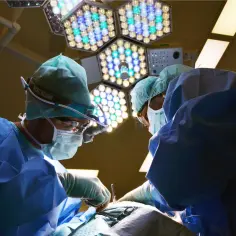Chirurdzy w maseczkach i czepkach podczas operacji pod jasnym światłem lampy zabiegowej.