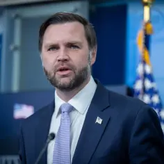 Mężczyzna w garniturze, z brodą i niebieskimi oczami, przemawia na tle flagi USA. To wiceprezydent USA.