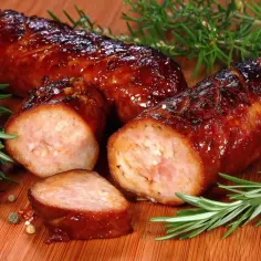 Soczysta kiełbasa z piekarnika, idealnie przypieczona, z gałązkami rozmarynu i ziarnami pieprzu na drewnianej desce.