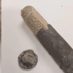 Zardzewiała metalowa kapsuła czasu z zrolowanym dokumentem w środku, obok leży zakrętka.