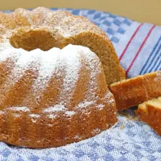 Babka wielkanocna posypana cukrem pudrem, obok pokrojone kawałki ciasta, na niebieskim ręczniku.
