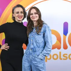 Ania Rusowicz, córka Niemena, w czarnej sukience i dżinsowym kombinezonie pozuje na tle logo Polsat.