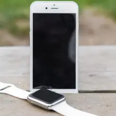 Biały smartwatch i smartfon leżą na drewnianym blacie. Dowiedz się, jak sparować zegarek z telefonem.