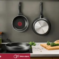 Dwie patelnie wiszą na ścianie, jedna z logo Tefal. Czy patelnie Tefal można myć w zmywarce? Na blacie leżą brokuły i przyprawy.