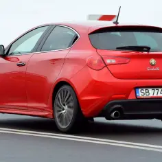Czerwona Alfa Romeo Giulietta w ruchu drogowym. Wiele osób szuka alfa romeo giulietta opinie przed zakupem.