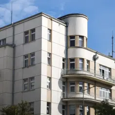 Charakterystyczna kamienica w Gdyni, stare miasto. Jasna fasada, zaokrąglony narożnik z balkonami, okna z żaluzjami.