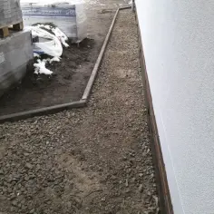 Ścieżka wysypana kruszywem dolomitowym obok budynku, z paletami materiałów budowlanych w tle.