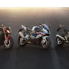 Trzy motocykle BMW S1000XR stoją na asfalcie o zachodzie słońca.