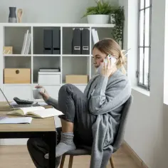 Kobieta rozmawia przez telefon, trzymając kubek. Na biurku laptop, notatnik i kalkulator. Czy to oznaka stagnacji, co to znaczy dla jej pracy?