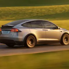 Srebrny Tesla Model X pędzi po drodze, otoczony złotymi polami.