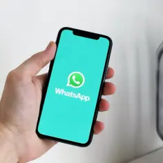 Dłoń trzyma smartfon z logo WhatsApp. Od ilu lat jest WhatsApp? Od 2009 roku, a to logo wciąż jest popularne.