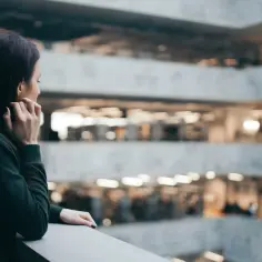 Kobieta zastanawia się, jak zostać psychologiem po innych studiach, patrząc na wielopoziomową architekturę budynku.