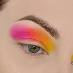 Oko z makijażem w stylu cut crease, z gradientem od fuksji przez pomarańcz do żółci.