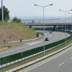 Szeroka droga krajowa z ruchem samochodowym i ciężarowym, znaki drogowe, zielone ekrany akustyczne i stacja Orlen.