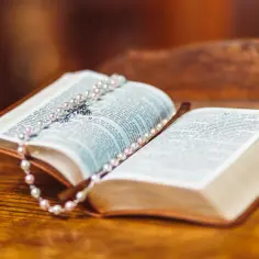 Otwarta Biblia, na której leży różaniec. Widoczny jest tekst Ewangelii św. Mateusza.