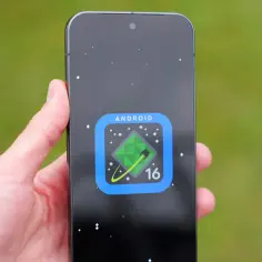 Dłoń trzyma smartfon z ikoną Android 16 na czarnym tle z gwiazdami.
