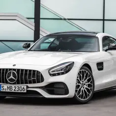 Biały Mercedes-AMG GTR z czarnym dachem i felgami, zaparkowany przed nowoczesnym budynkiem.