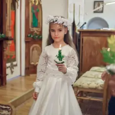 Dziewczynka w białej sukni i wianku, trzymająca świecę, przygotowuje się do komunii. Ma około 9 lat.