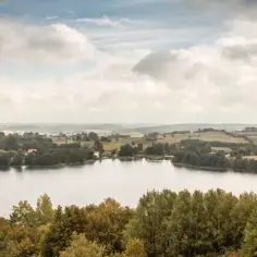 Spokojne **chańcza jezioro** otoczone zielonymi lasami i pagórkami. Na horyzoncie widać domy i pola.