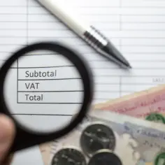 Pod lupą widać rachunek z pozycjami: Subtotal, VAT, Total. Obok leżą pieniądze, jakby art. 96 ust. 6-8 regulował podatki.