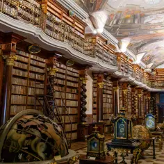 Wnętrze Biblioteki Narodowej Republiki Czeskiej z bogato zdobionymi regałami, globusami i malowanym sufitem.