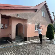 Mężczyzna myje elewację budynku myjką ciśnieniową.