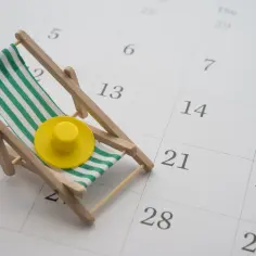 Miniaturowa leżanka z żółtym kapeluszem na kalendarzu. Zastanawiasz się, jak sprawdzić staż pracy do urlopu?