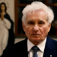Starszy mężczyzna w garniturze patrzy wprost. W tle widać postać Matki Boskiej. Proście, a będzie wam dane.
