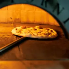 Piec opalany drewnem, w którym piecze się pyszna pizza rzymska. Gorące wnętrze pieca otacza okrągły placek z serem i dodatkami.